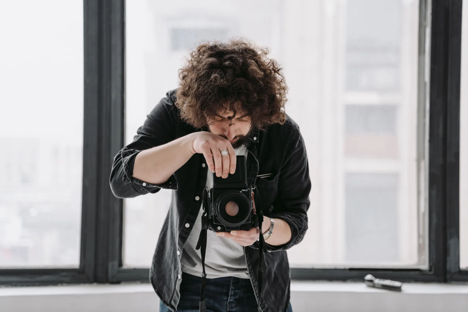 A photographer looking down into a medium format camera beside a large window