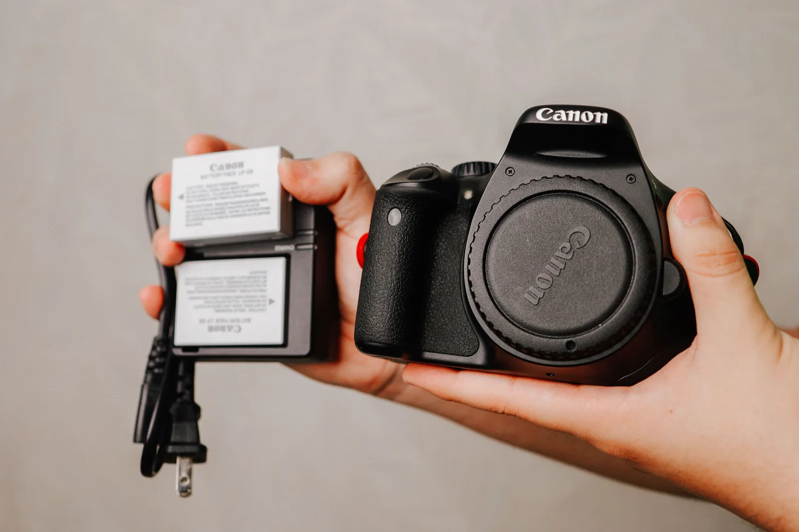 A camera body held beside its spare battery and charger before packing