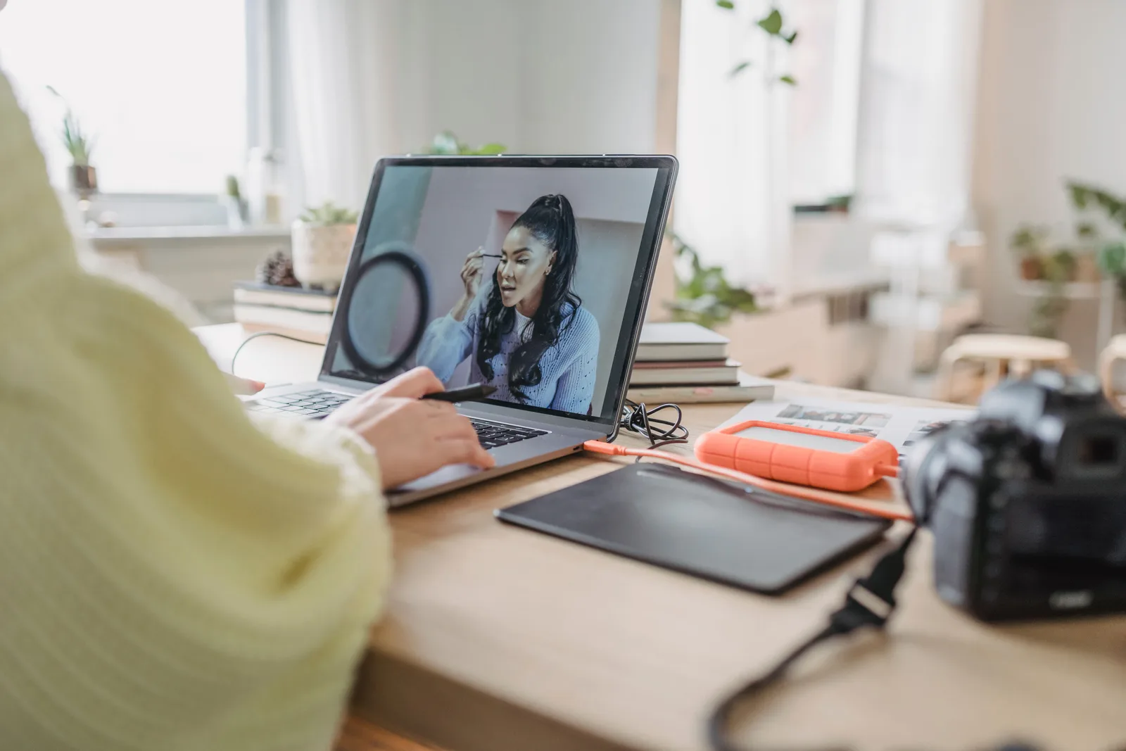 A photographer retouching a portrait on a laptop with a drawing tablet and camera on the desk