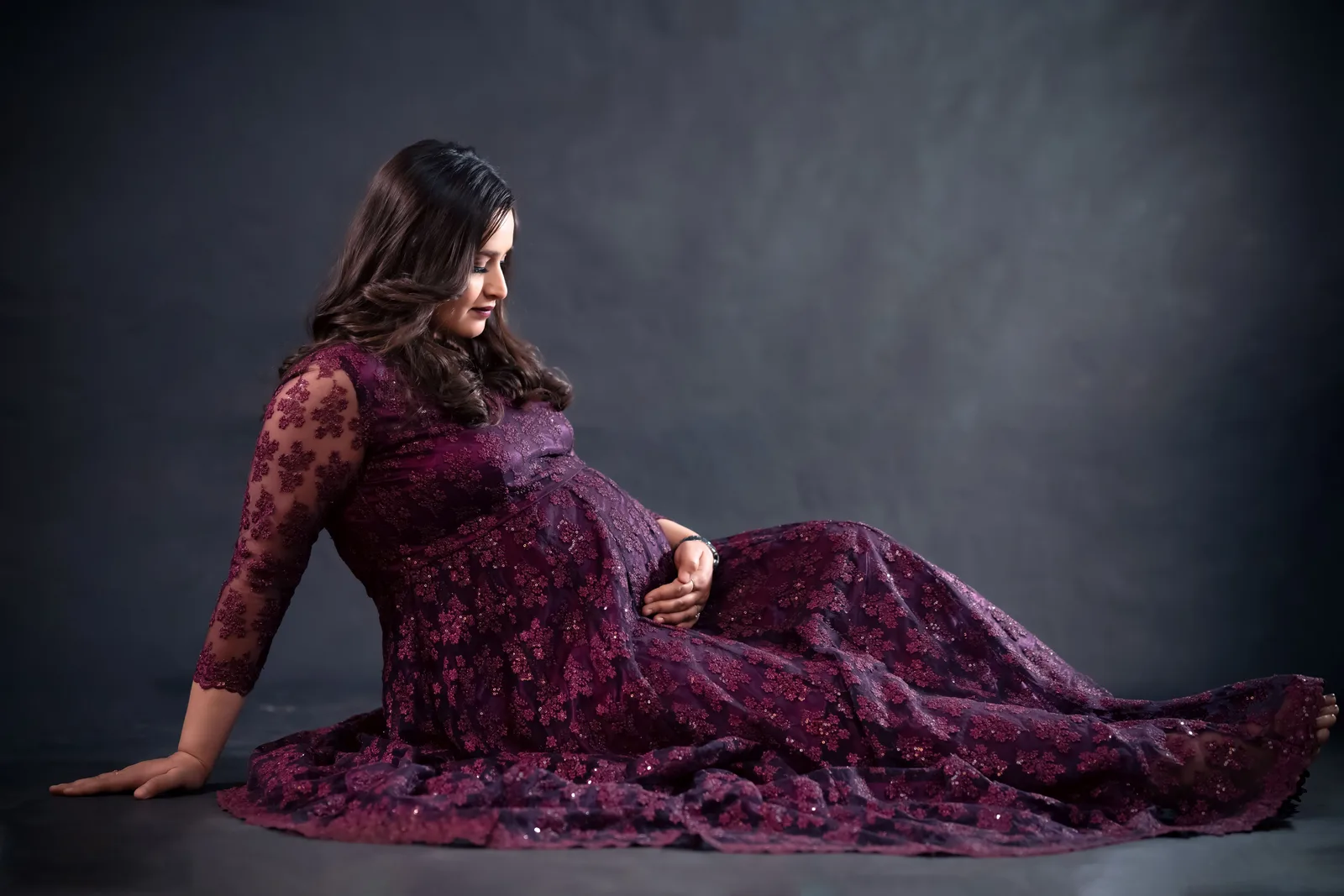 A pregnant woman in a flowing gown holding her bump during a maternity photo session