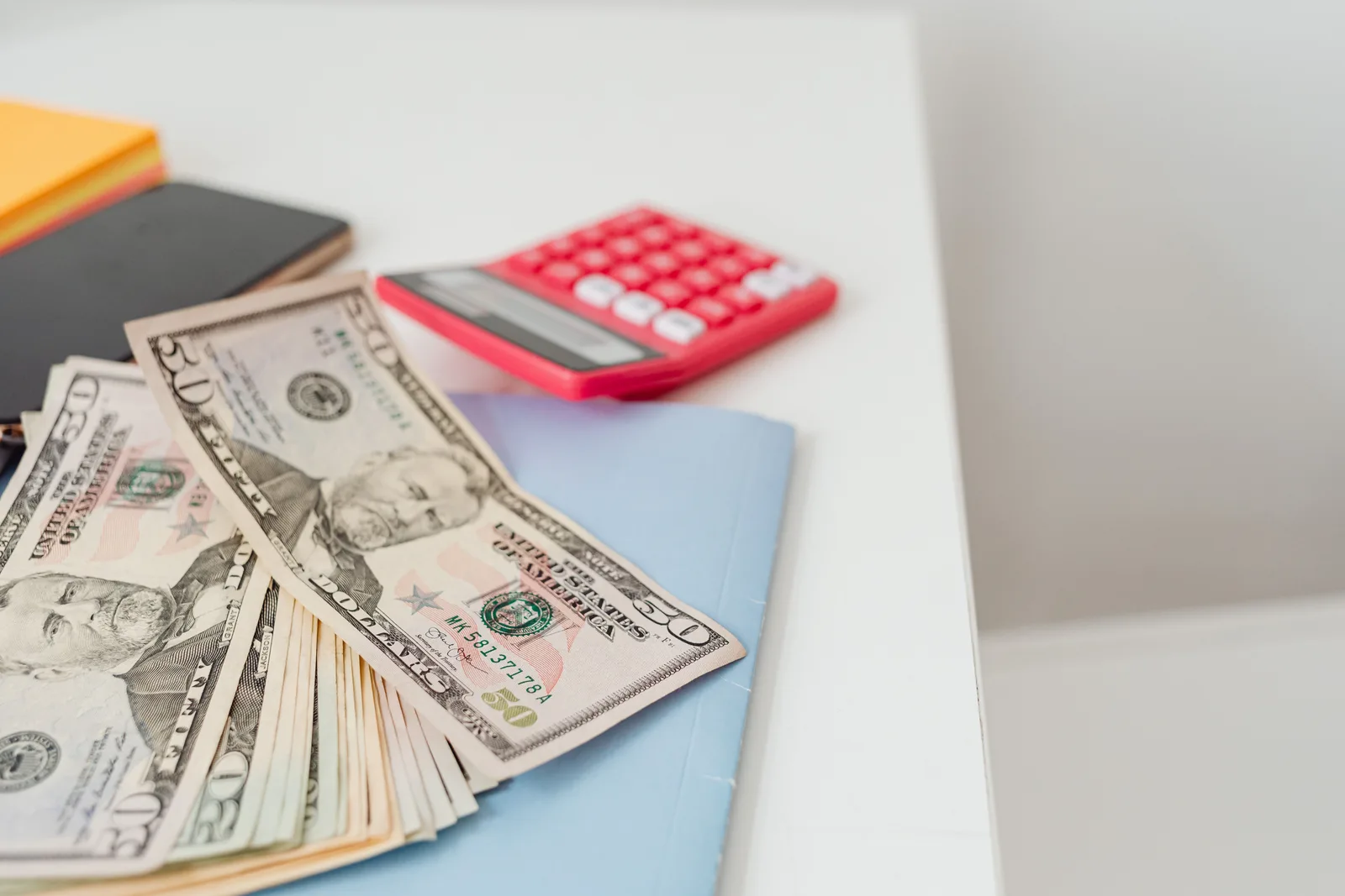Banknotes and a calculator on a desk beside a notebook
