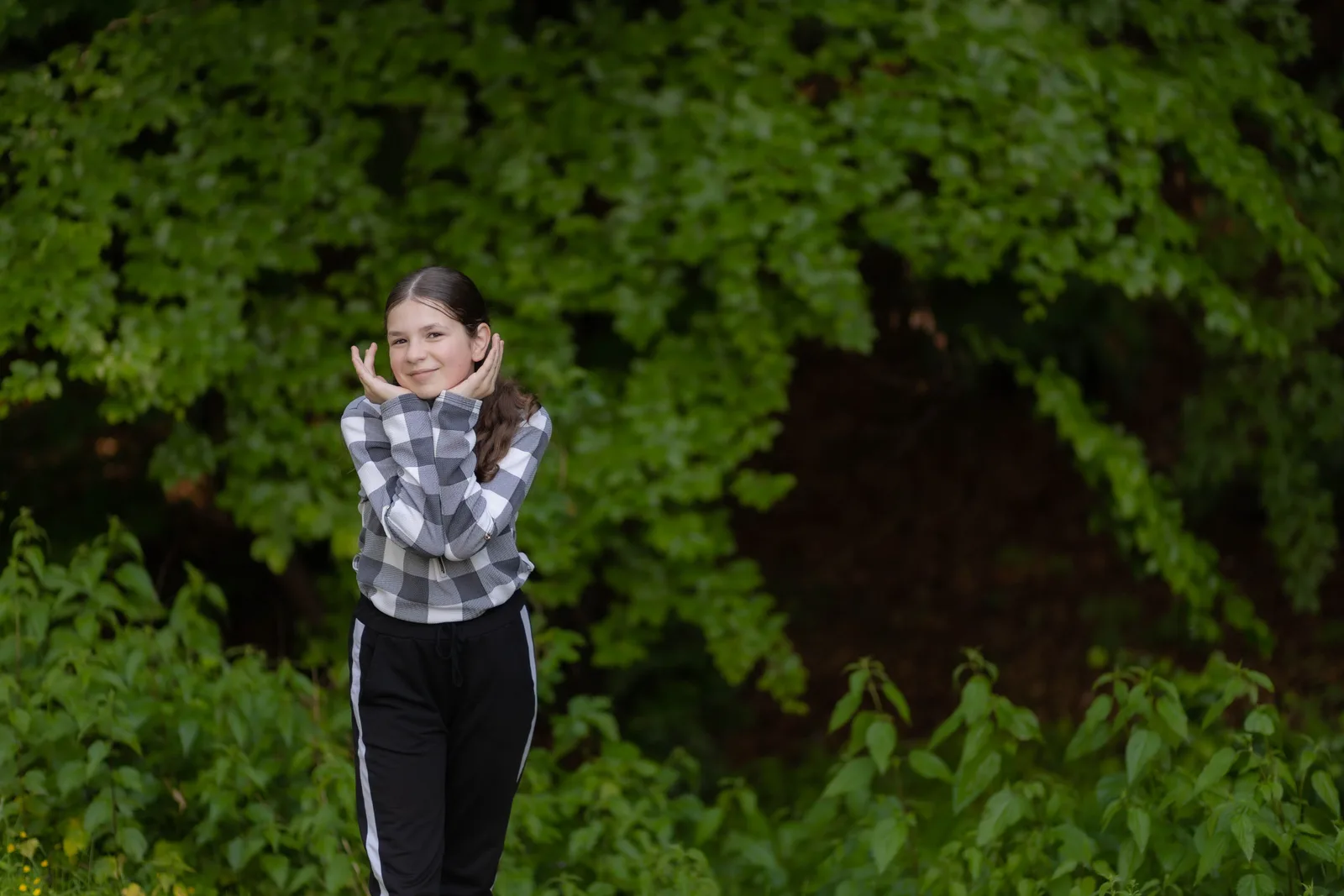 A teenage girl in a checked shirt posing in front of green foliage during an outdoor portrait session