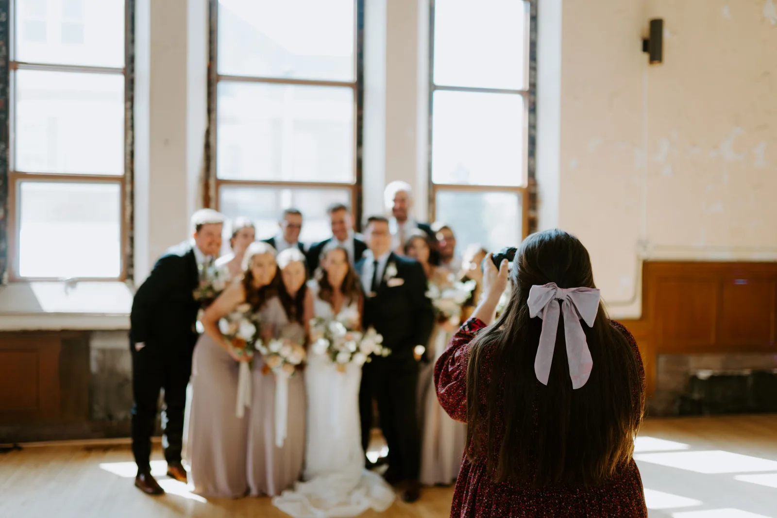A photographer photographing the wedding party in a hall with tall windows