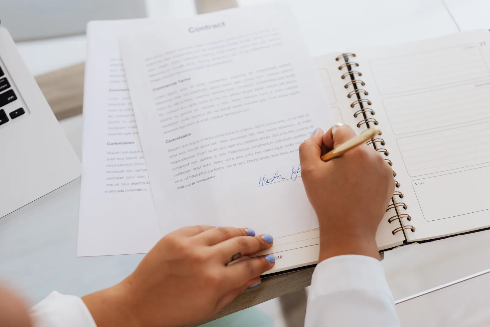 A printed contract being signed at a desk beside an open notebook