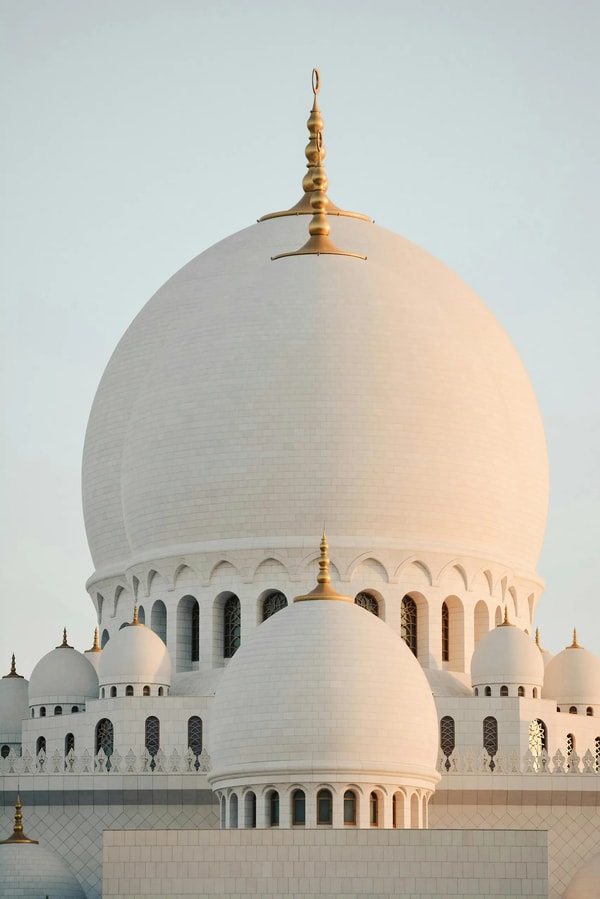 White marble domes and gold finial of a grand mosque against a pale sky