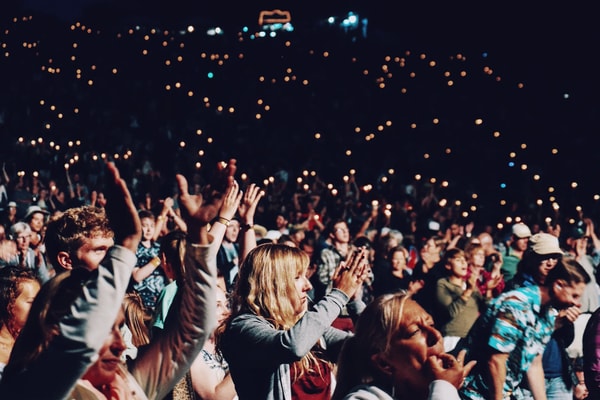 A crowd cheering and singing along with arms raised, hundreds of small lights behind them