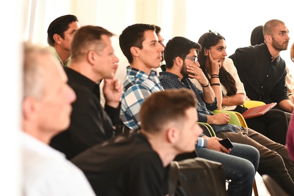 A row of attendees leaning forward to listen, one with a hand over his mouth