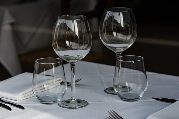 Empty wine and water glasses on a white tablecloth, the room dark behind them