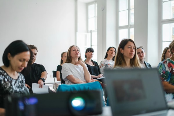 Workshop attendees in a bright room with tall windows, a projector glowing in front of them