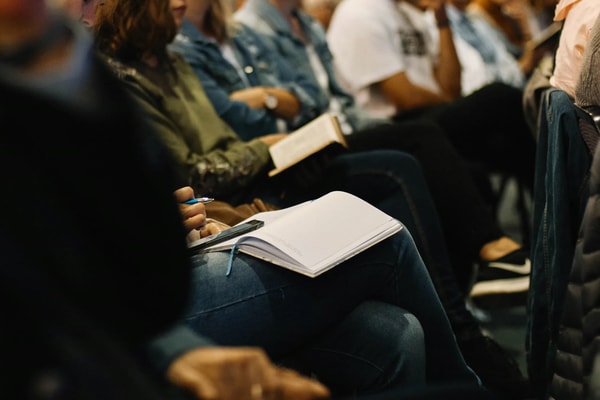 Close-up of an attendee’s open notebook and pen on her lap in a row of seats