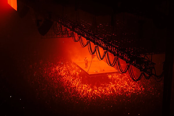 A packed arena floor glowing red under a suspended lighting rig