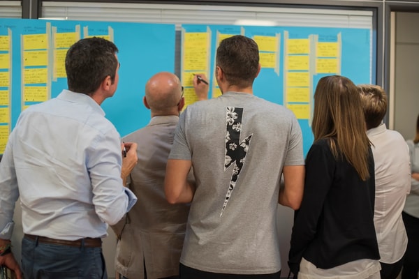 A group standing at a blue wall of yellow sticky notes, one of them writing