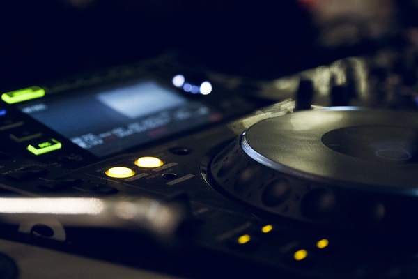 Close-up of a DJ turntable and mixer lit by small green and amber lights