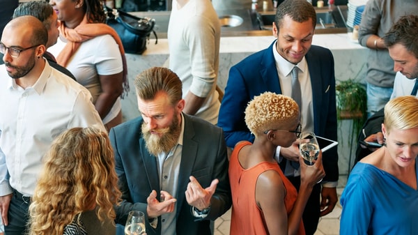 Guests talking in a tight circle at a standing reception, glasses and a tablet in hand