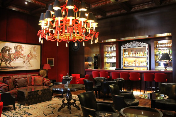 A bar lounge with a red chandelier, leather armchairs and a row of red bar stools