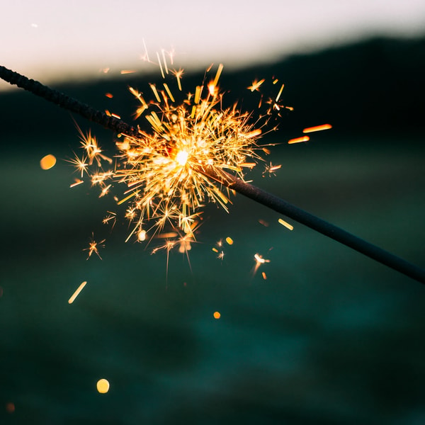 A lit sparkler throwing orange sparks against a dark green background