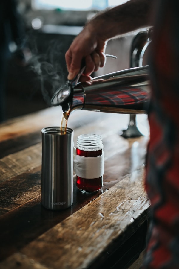 Coffee poured from a steel pot into a tumbler on a wooden bar