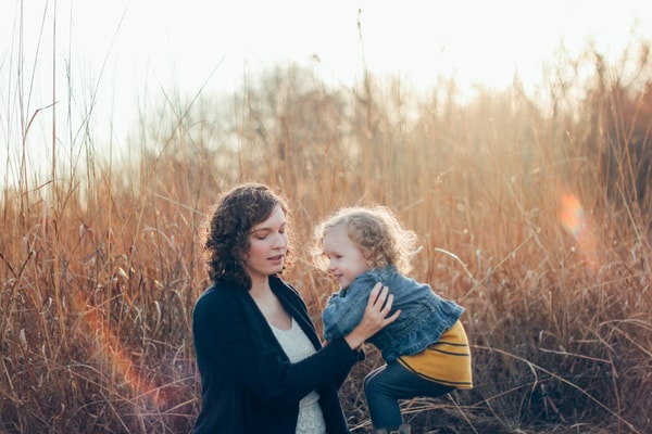 Mother lifting her laughing toddler in tall autumn grass, low sun behind them