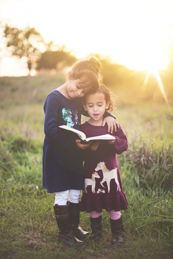 Two sisters reading a book together in a meadow at sunset
