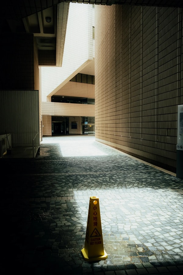 Sunlit alley between tiled buildings, a lone yellow wet floor cone on the cobblestones