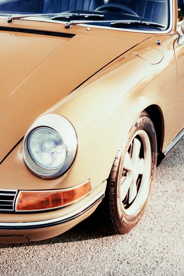Front wheel and headlight of a vintage tan sports car parked on gravel