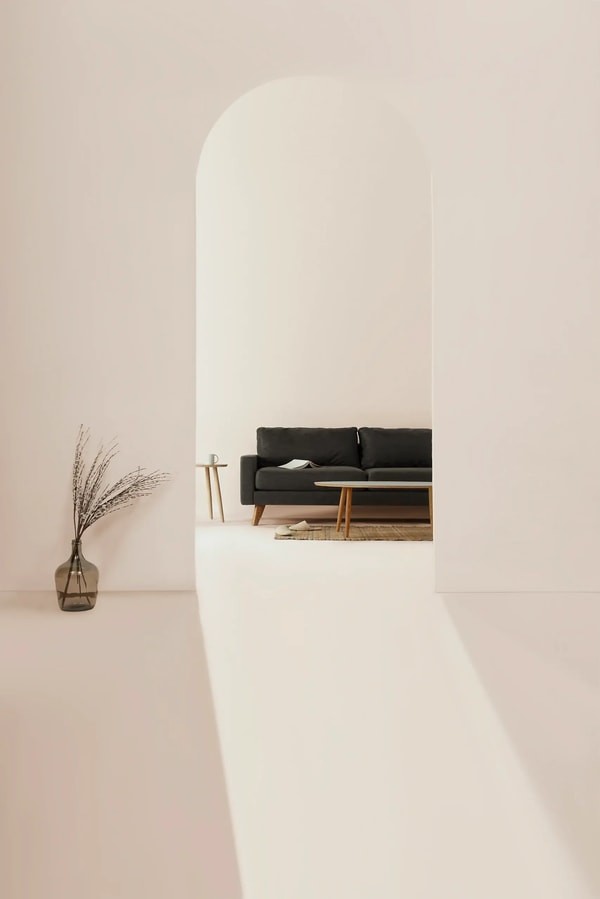 Minimal white interior with an arched alcove, a dark sofa and dried grasses