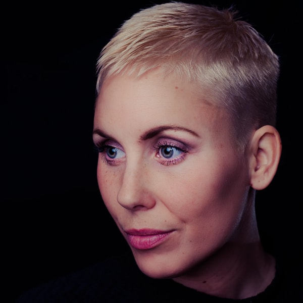 Close studio headshot of a woman with a short platinum crop, lit softly against black