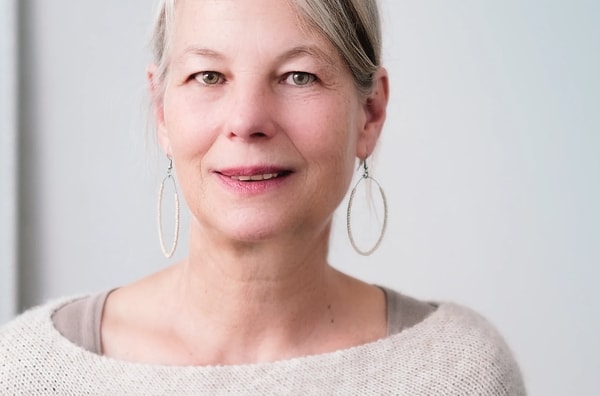 Headshot of a smiling woman with grey-blonde hair and hoop earrings on a white backdrop