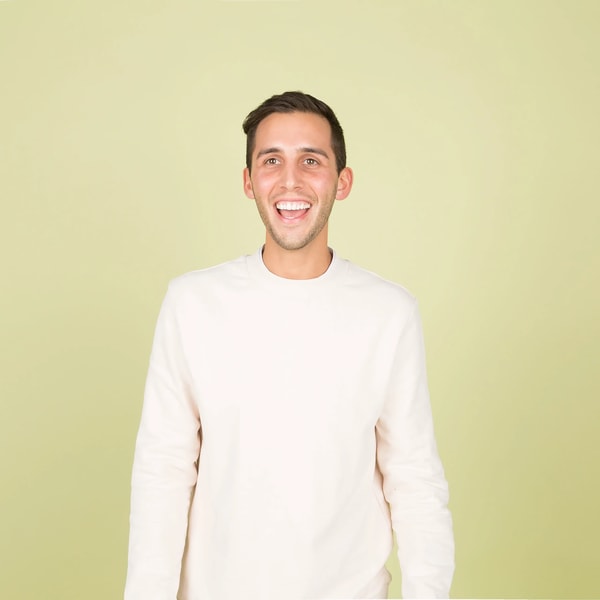 Young man in a cream sweater laughing against a pale green studio backdrop