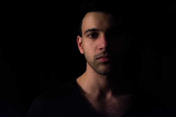 Young man with dark hair lit by a single light, most of his face in shadow