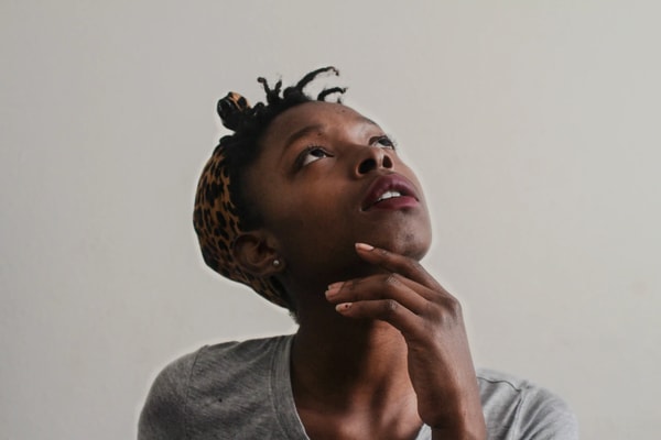Woman with a leopard print headband resting her chin on her hand, looking up, on a plain wall