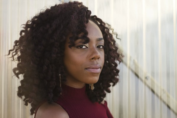 Woman with long dark curls in a burgundy top looking straight at the camera