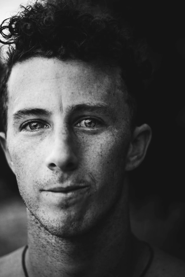 Black and white portrait of a young man with curly hair and freckles, lit from one side