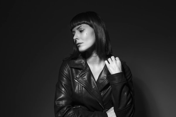 Black and white studio portrait of a woman with a fringe in a leather jacket, eyes lowered