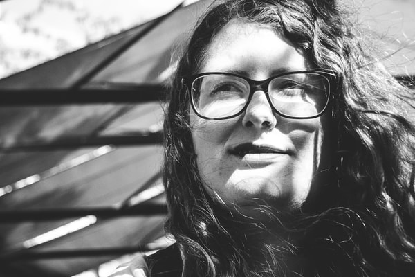 Black and white portrait of a woman in thick glasses with long wavy hair, in bright sun