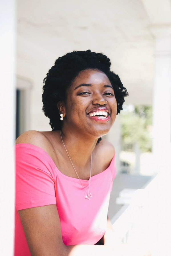 Laughing woman in a pink off-shoulder top leaning on a white porch rail