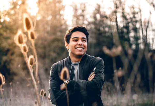 Smiling young man with crossed arms in a field of dry teasels at golden hour