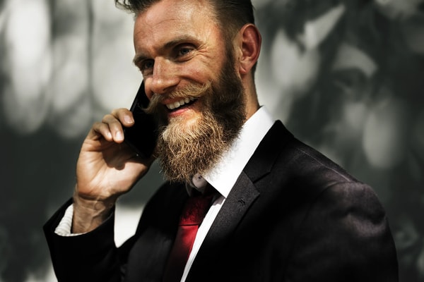 Laughing bearded man in a suit and red tie talking on his phone