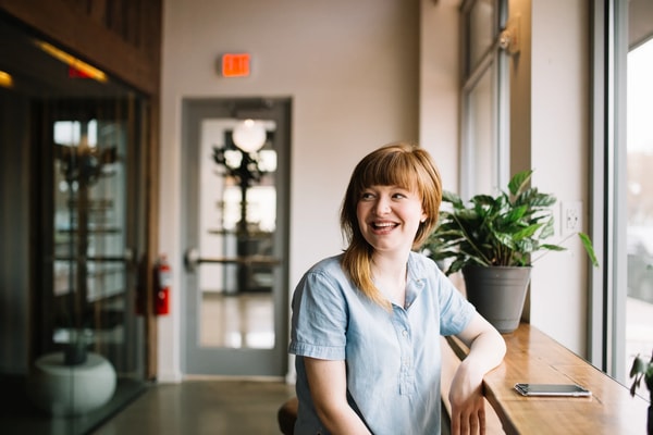 Laughing woman in a light blue shirt at a window counter in a bright café
