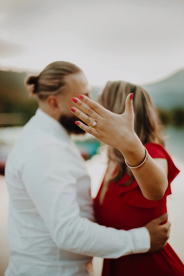 Couple embracing outdoors, an engagement ring on the hand resting at his shoulder