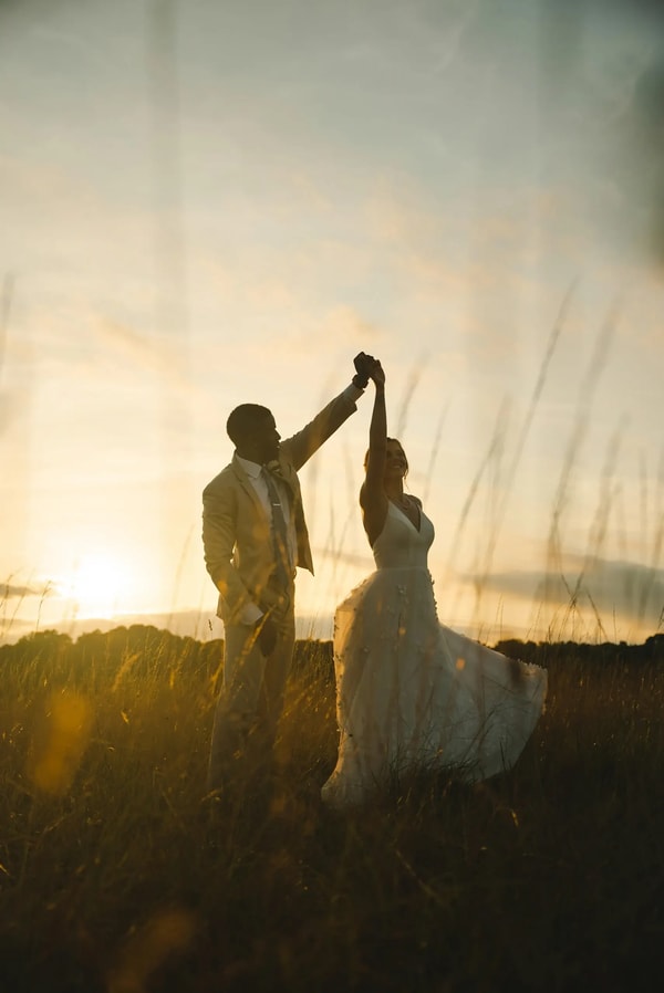 Silhouetted couple dancing in tall grass at golden hour, sun flaring behind them