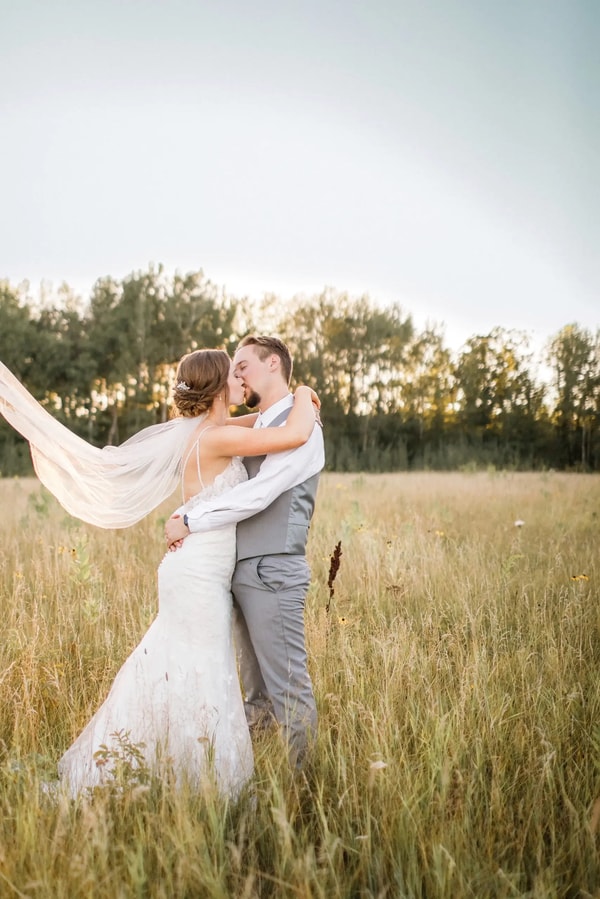 Couple embracing in a meadow at dusk, the veil floating out behind them