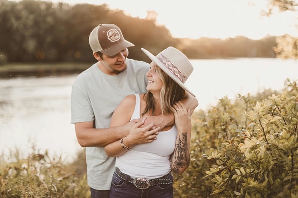 Couple in caps and a straw hat laughing together by a river at golden hour