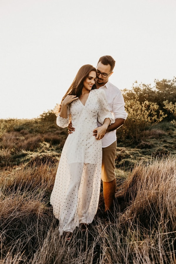 Couple embracing in tall golden grass, the bride in a lace gown
