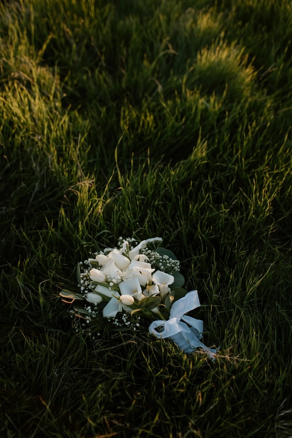 A white calla lily bouquet tied with blue ribbon lying in deep grass