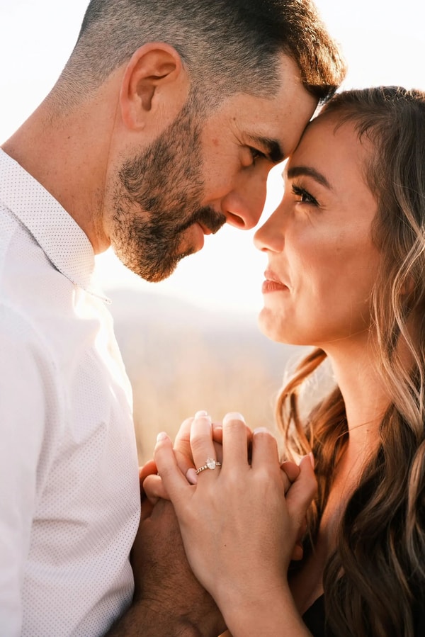 Couple leaning together in backlit sun, her ring hand resting on his