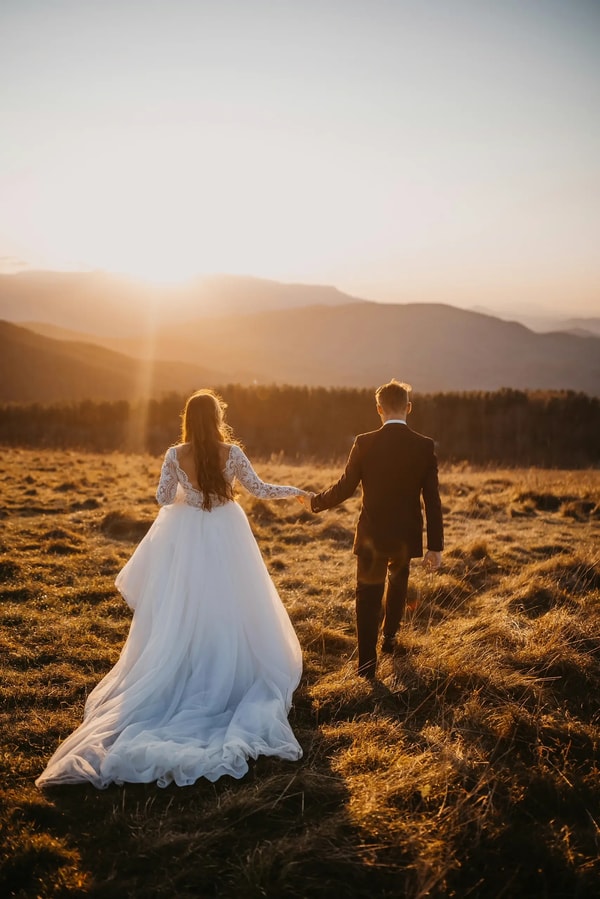 Bride and groom walking hand in hand through a mountain meadow at sunrise