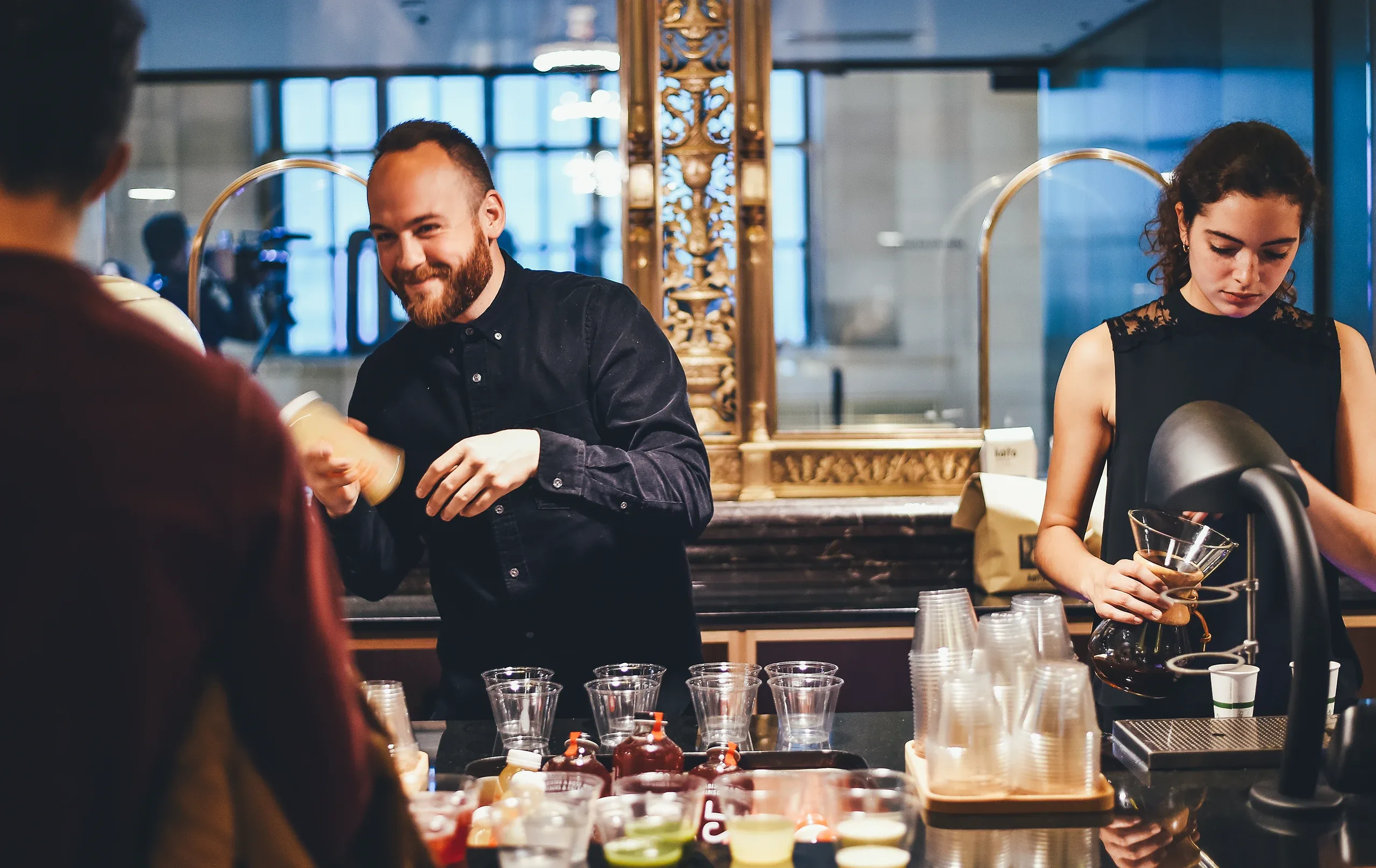 A bartender laughing with a guest while a colleague pours drinks behind a busy bar