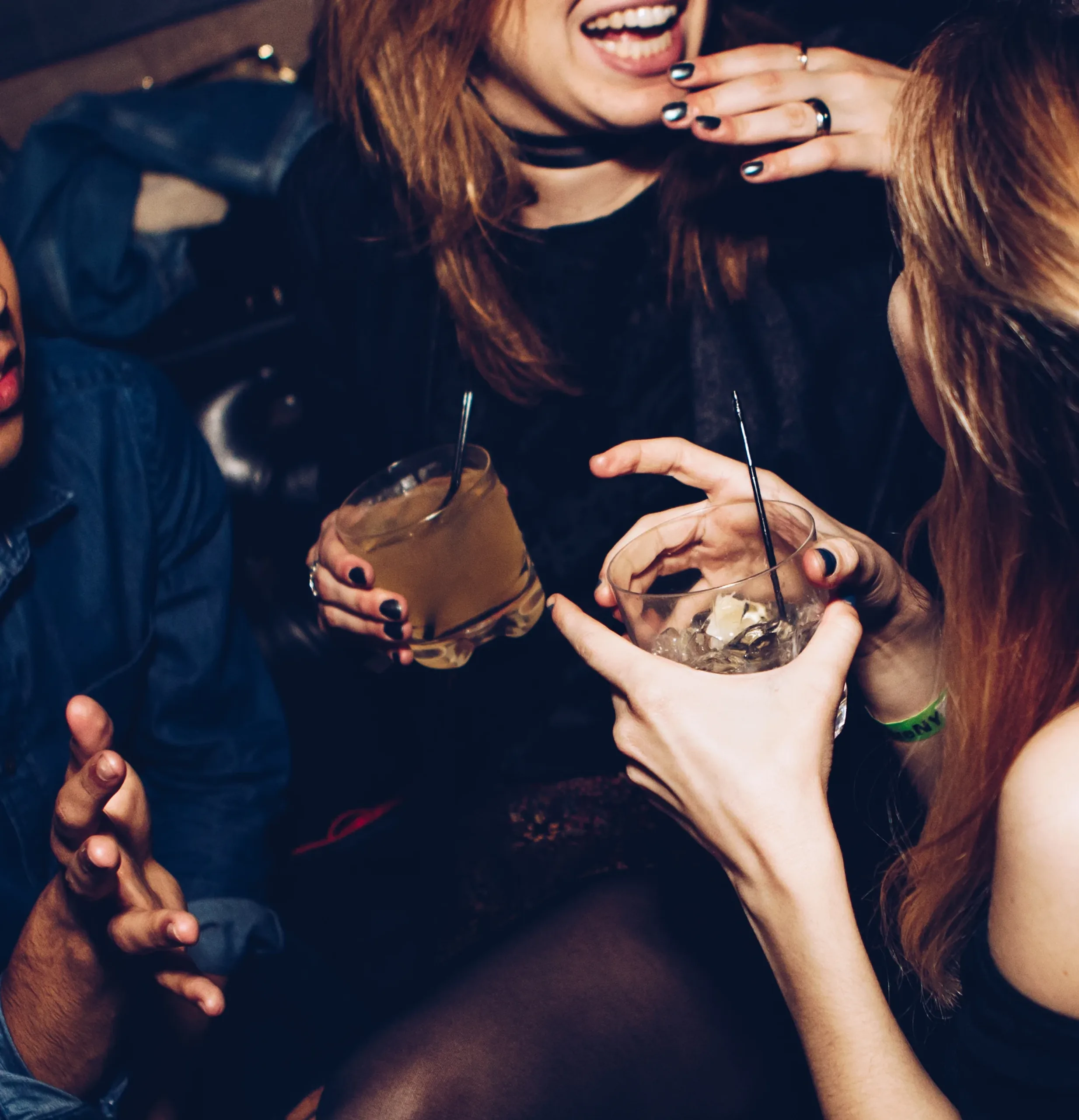 Two women laughing close together with cocktails in hand in the dark of a club