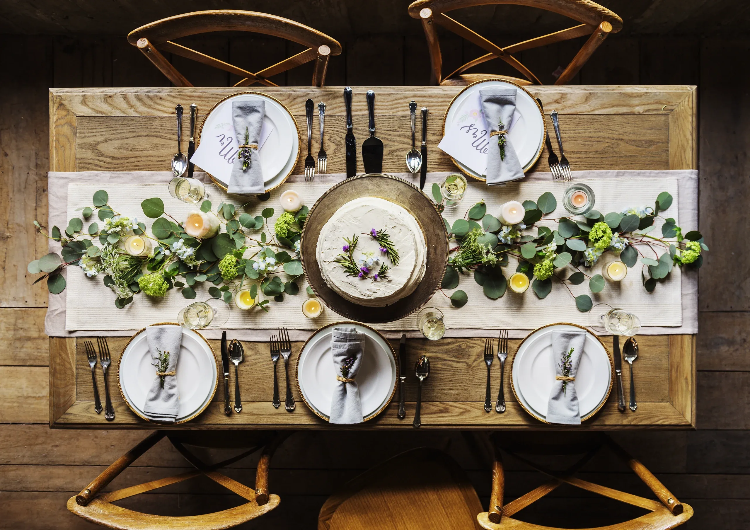 Overhead view of a set dinner table with greenery down the middle and a napkin on each plate
